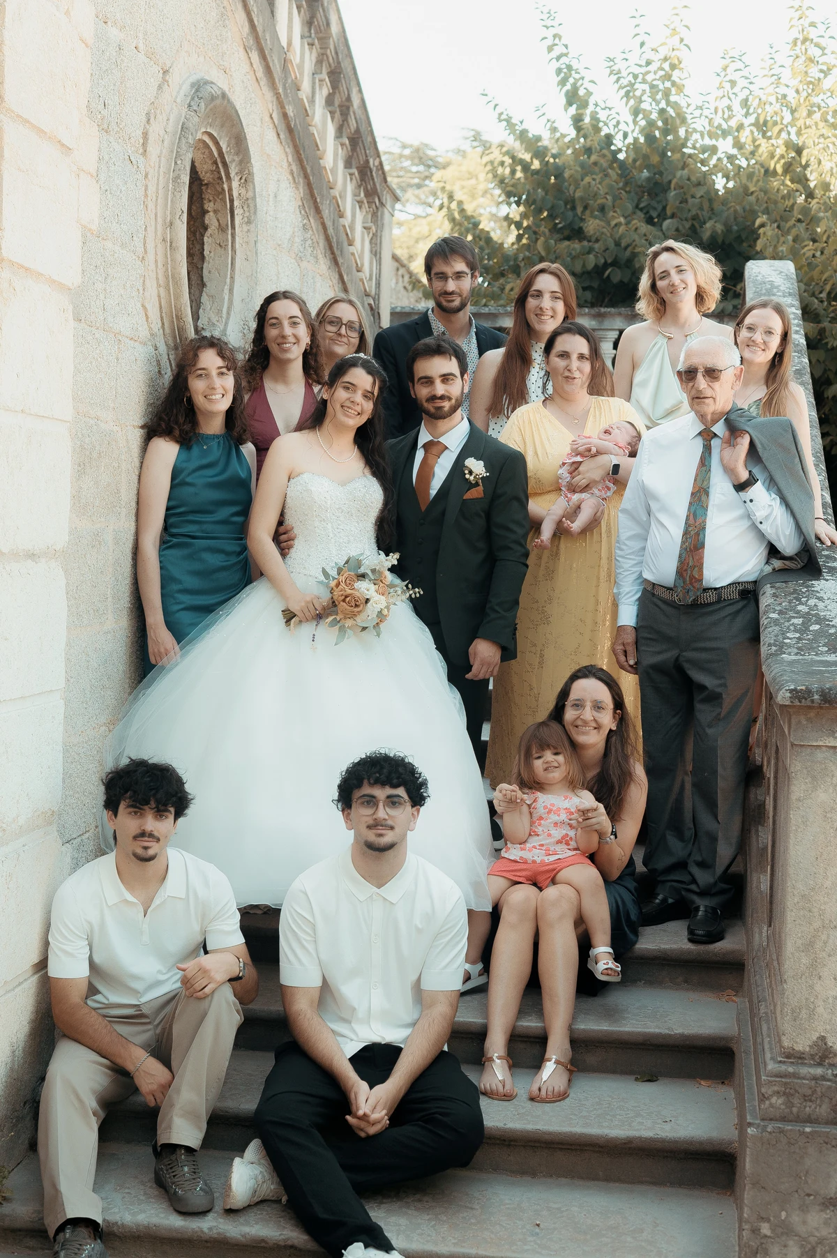 Photo de famille multigénérationnelle sur escalier en pierre avec mariés au centre, mariage au Oullins-Pierre-Bénite