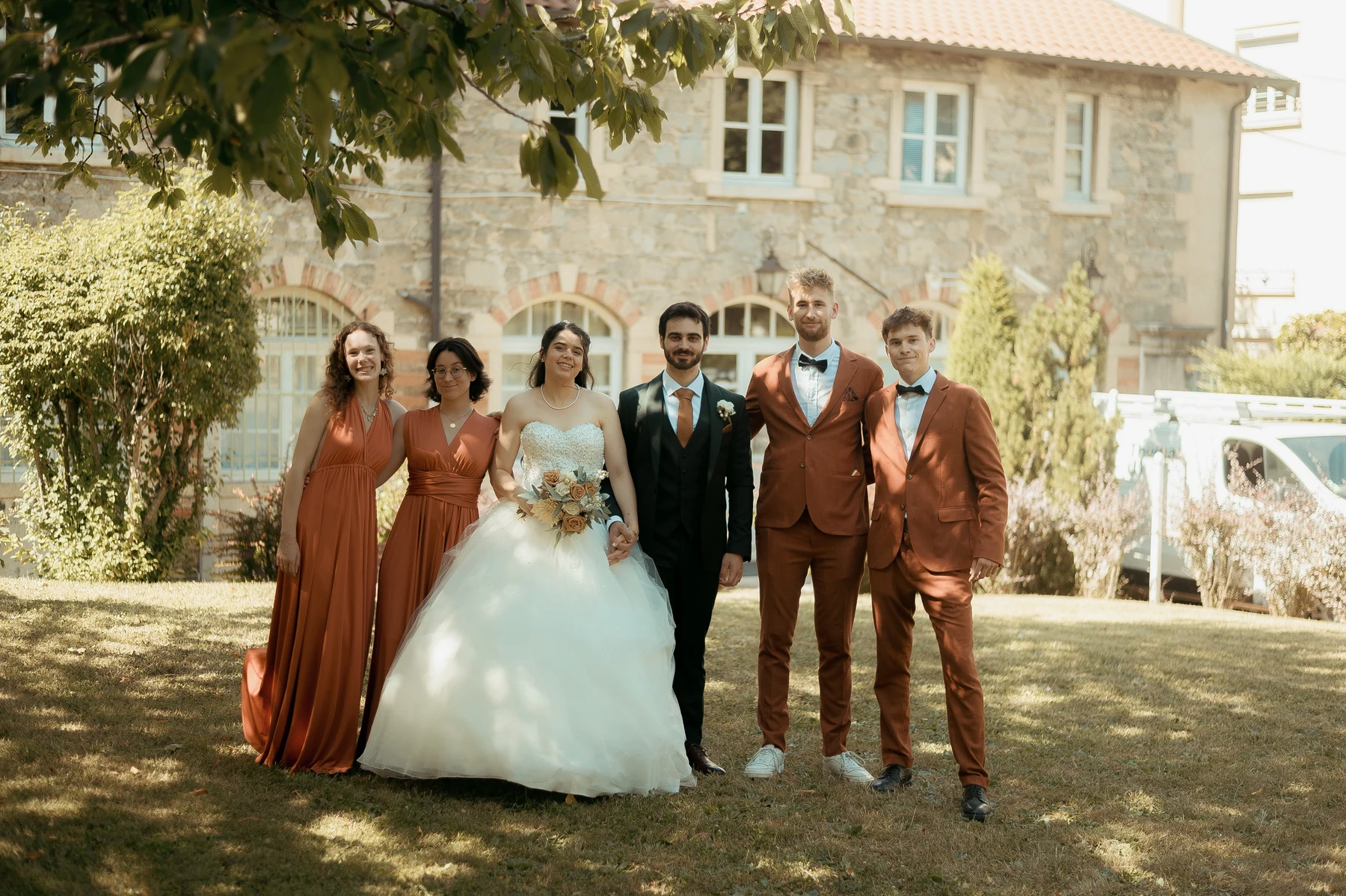 Mariés et quatre témoins en tenues terracotta devant bâtisse en pierre, mariage au Oullins-Pierre-Bénite