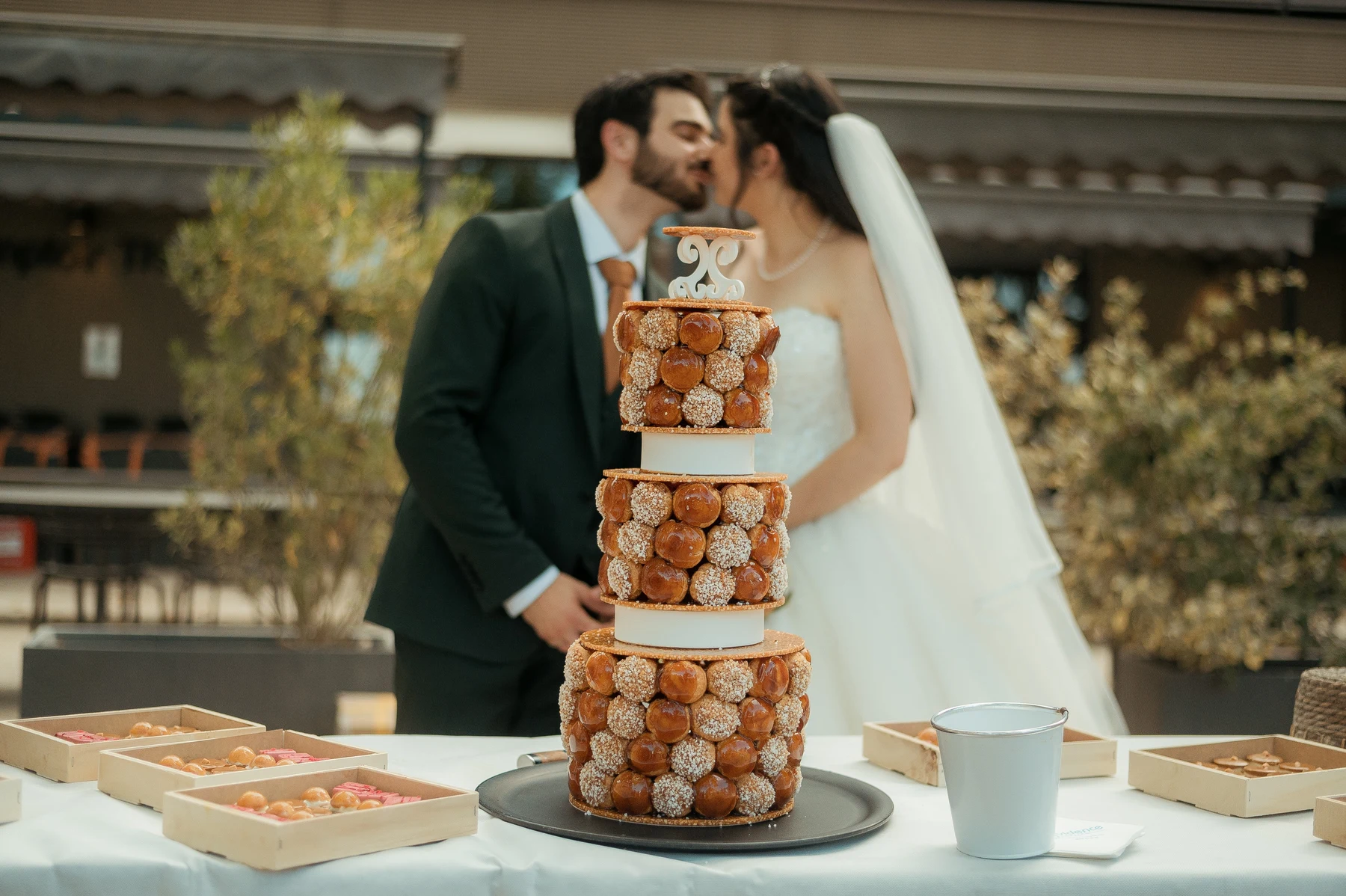 Pièce montée de choux dorés avec mariés s'embrassant en arrière-plan, mariage au Oullins-Pierre-Bénite
