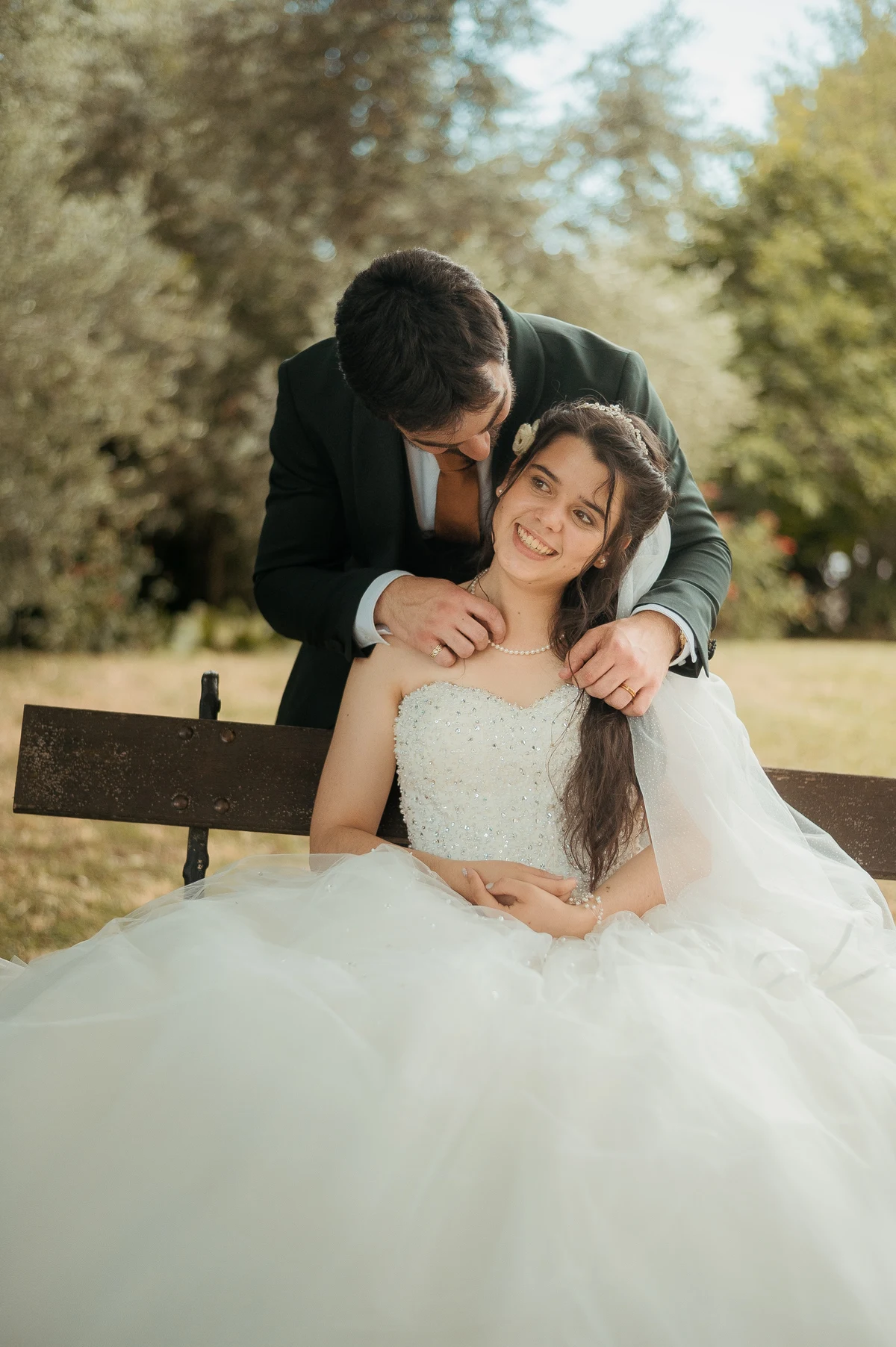 Marié coiffant la mariée assise sur banc dans parc arboré, mariage au Oullins-Pierre-Bénite
