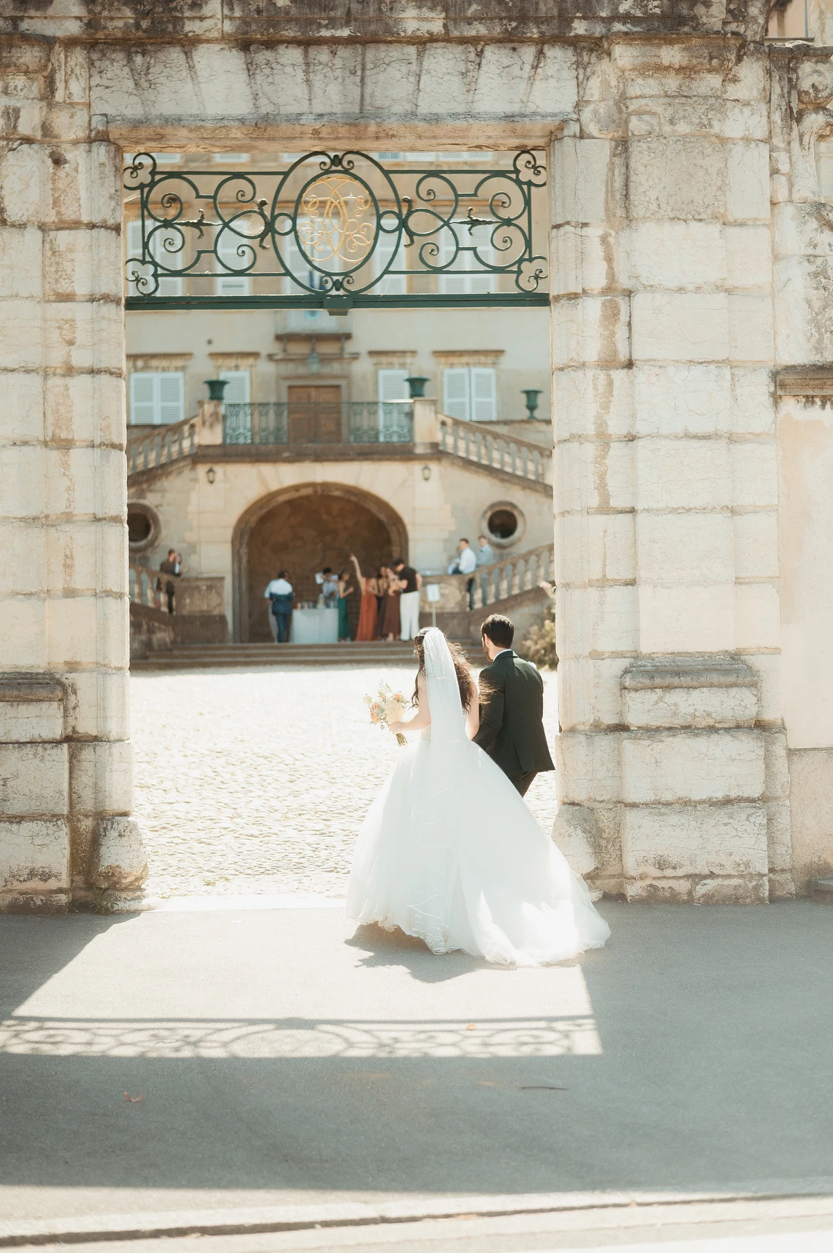 Mariés franchissant un portail en pierre vers le château pour le vin d'honneur, mariage au Oullins-Pierre-Bénite
