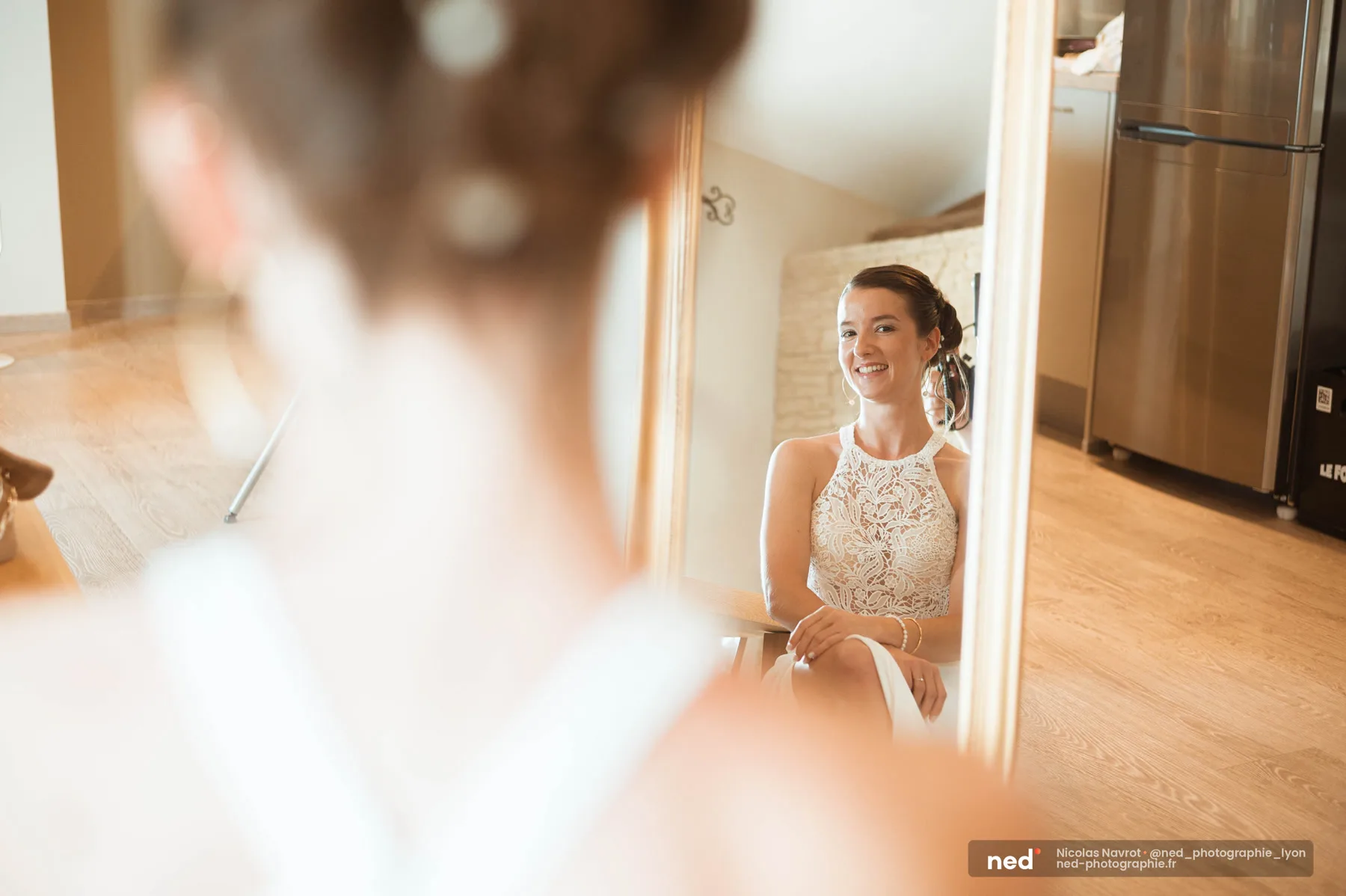 La mariée sourit en se découvrant dans le miroir à la fin de ses préparatifs, mariage au Domaine de Bellevue