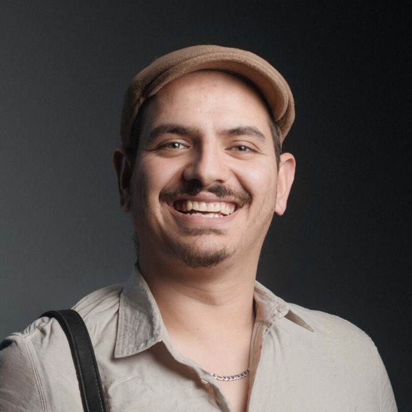 Homme en casquette beige et chemise claire sourit face à la caméra sur fond gris neutre c'est Nicolas Navrot