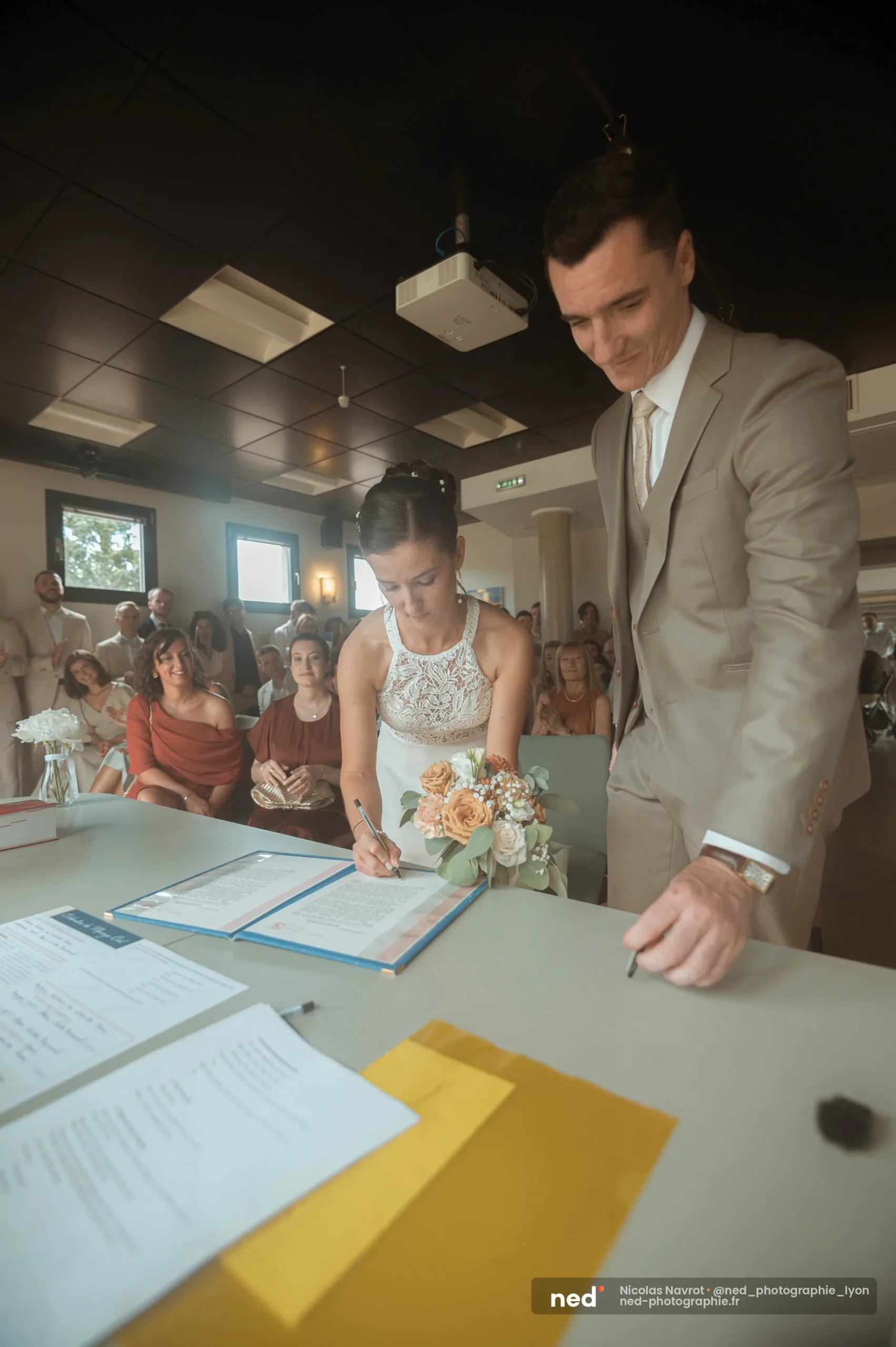 La mariée signe le registre de mariage à la mairie sous le regard du marié