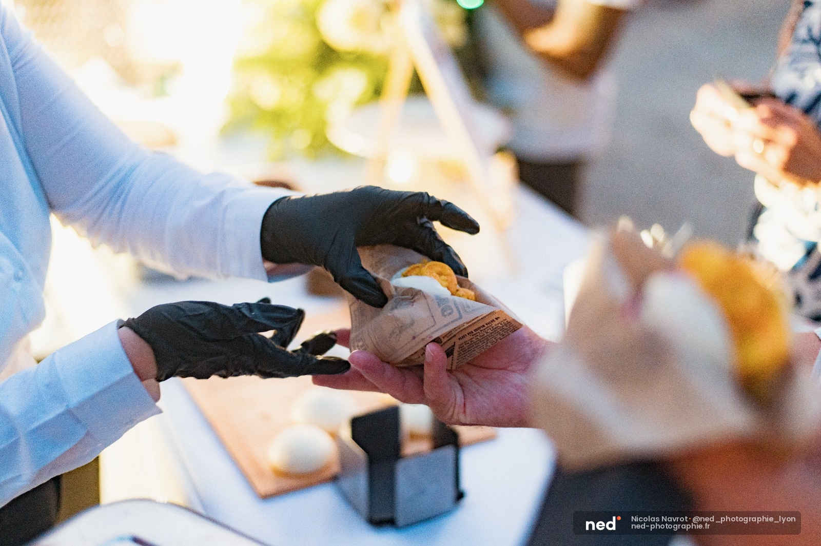 Participant en gants noirs examine un sandwich pendant un atelier photo, autres personnes autour d'une table de travail