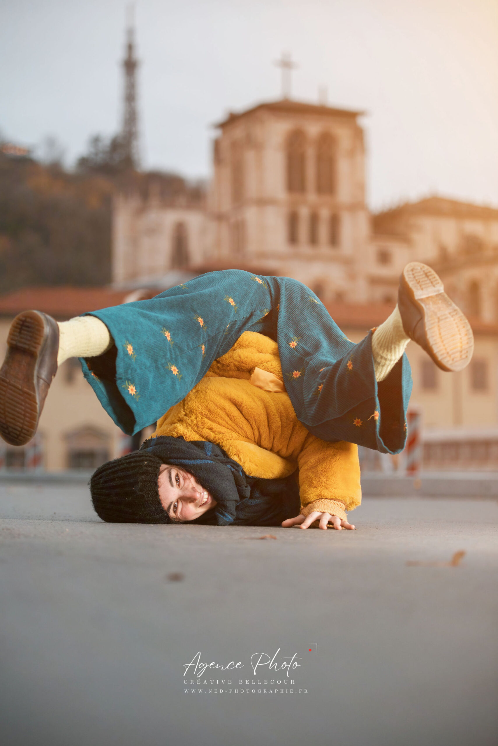 Enfant en pull jaune et bonnet noir fait l'équilibre sur ses mains devant la basilique Notre-Dame de Fourvière à Lyon