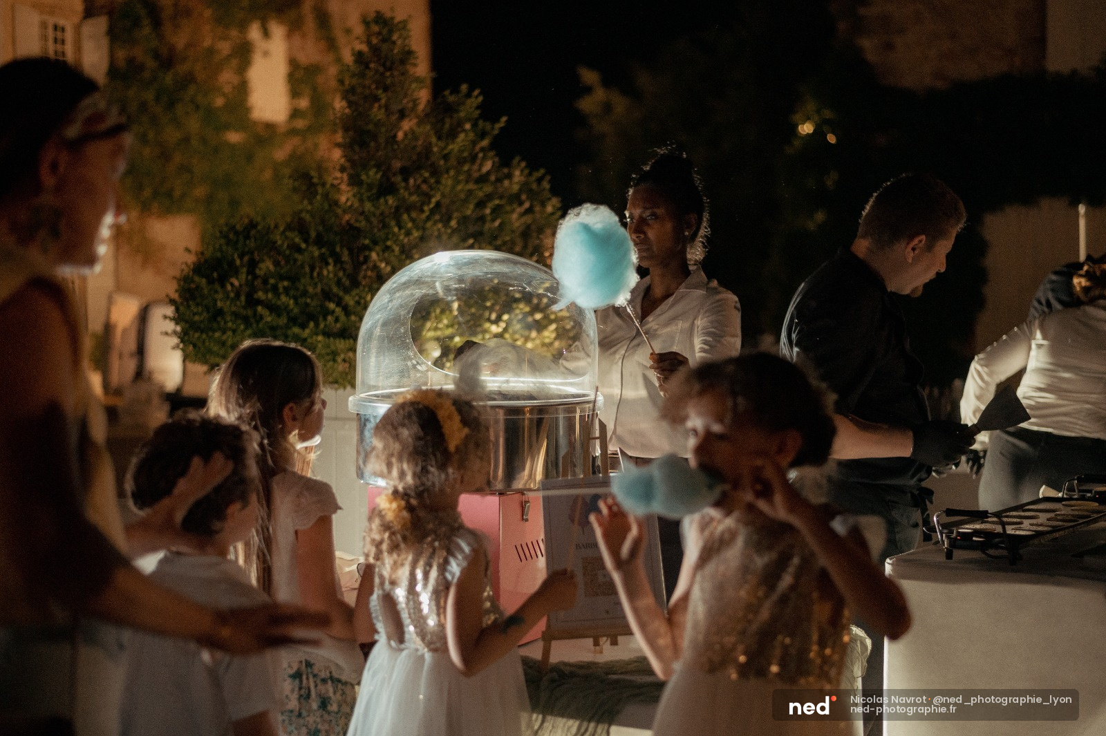 Enfants et adultes autour d'une machine à barbe à papa lumineuse lors d'un événement en extérieur la nuit