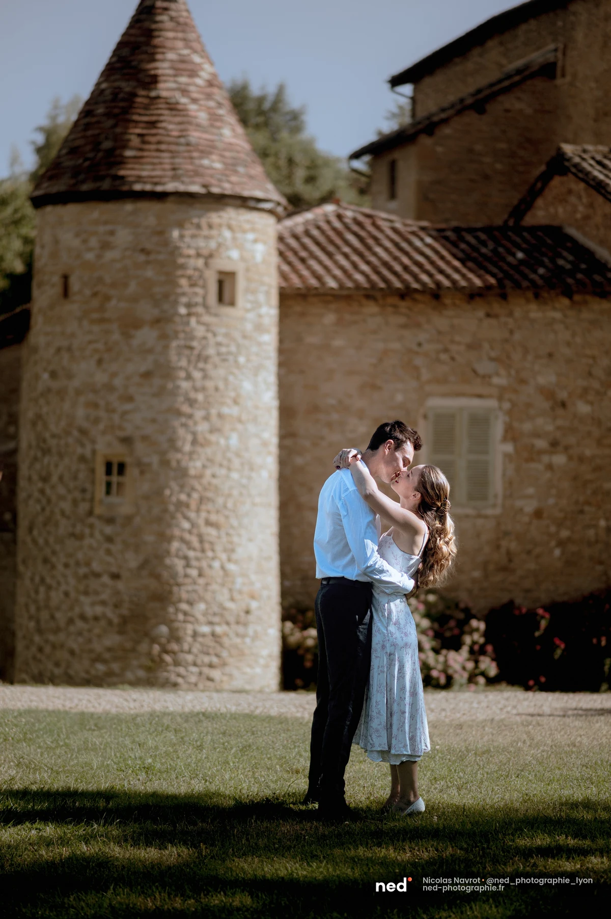 Couple qui s'embrasse devant une tour en pierre d'un château du Beaujolais, séance photo de couple au Château du Sou