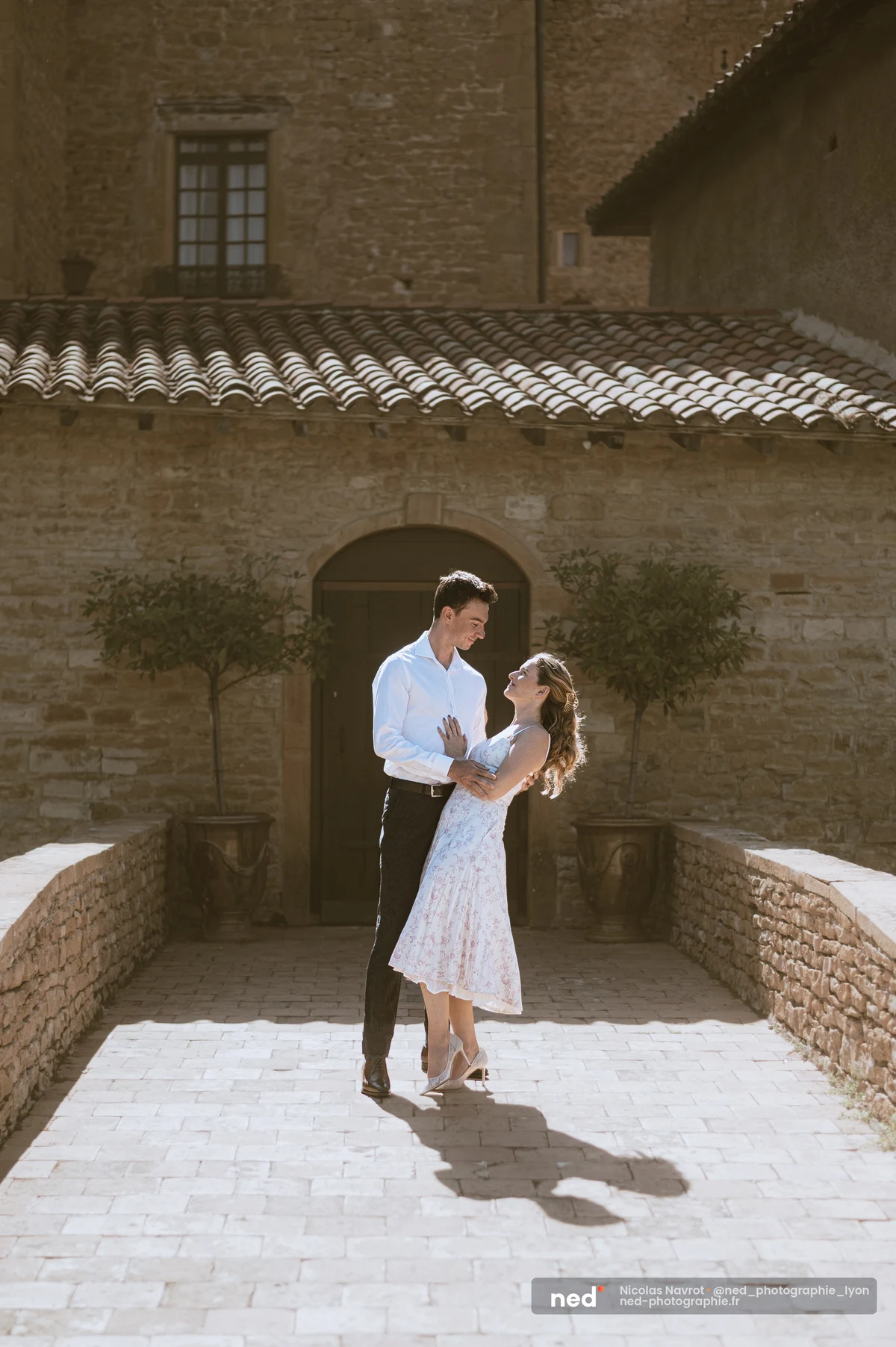 Couple enlacé devant un mas en pierre, allée pavée ensoleillée, oliviers., séance photo de couple au Château du Sou