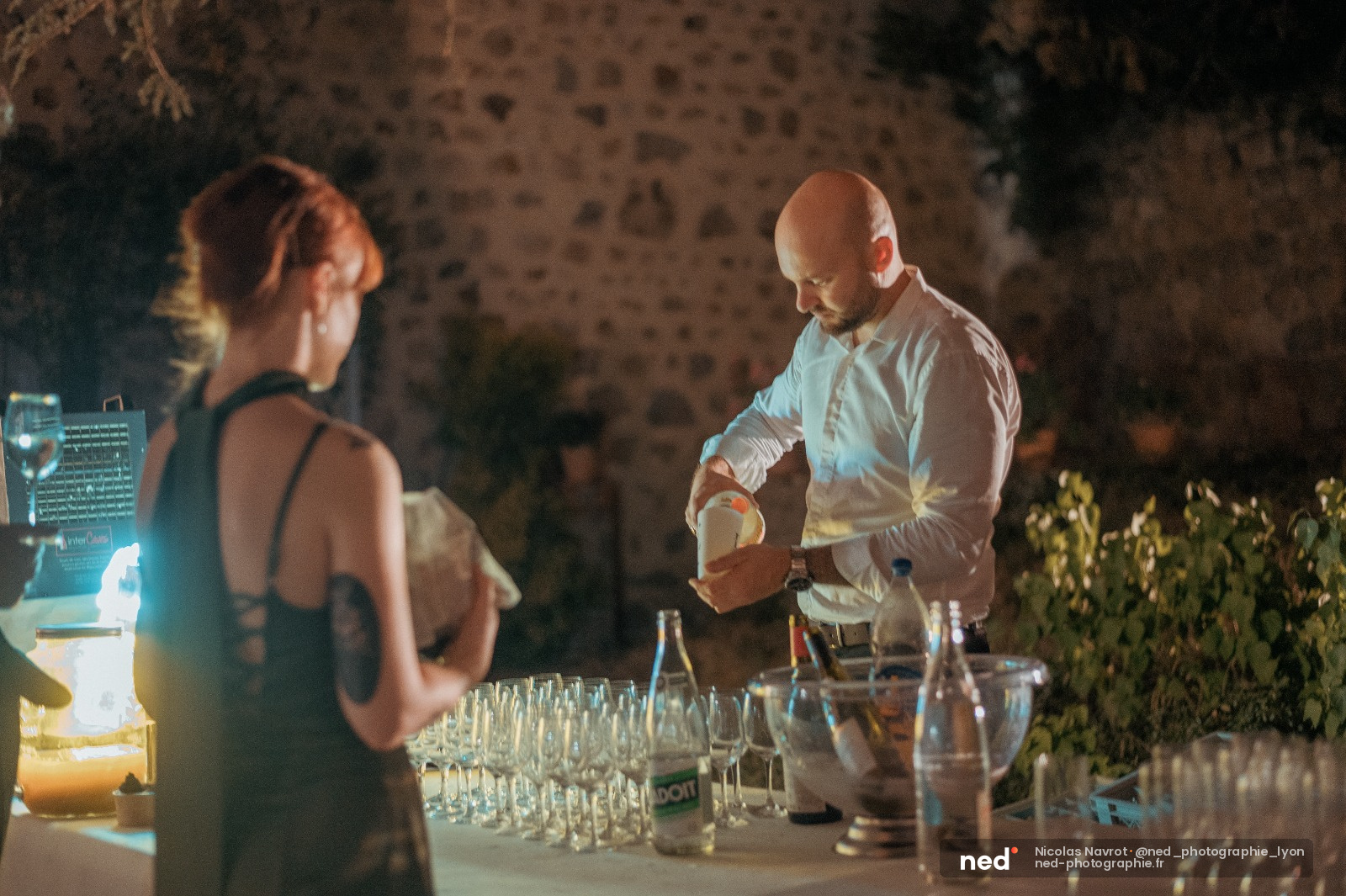 Homme en chemise blanche et femme en robe noire se regardent à table lors d'une réception de mariage en soirée