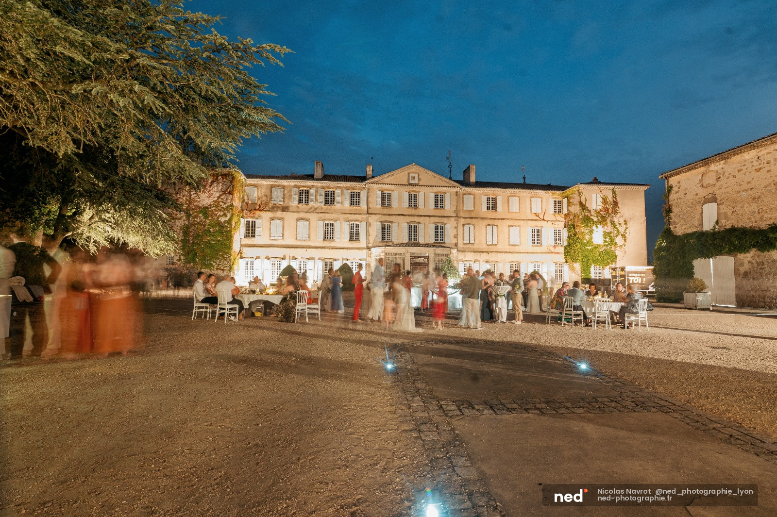 Invites en tenue de soiree danent et discutent dans la cour eclairee d'un chateau provencal illumine la nuit