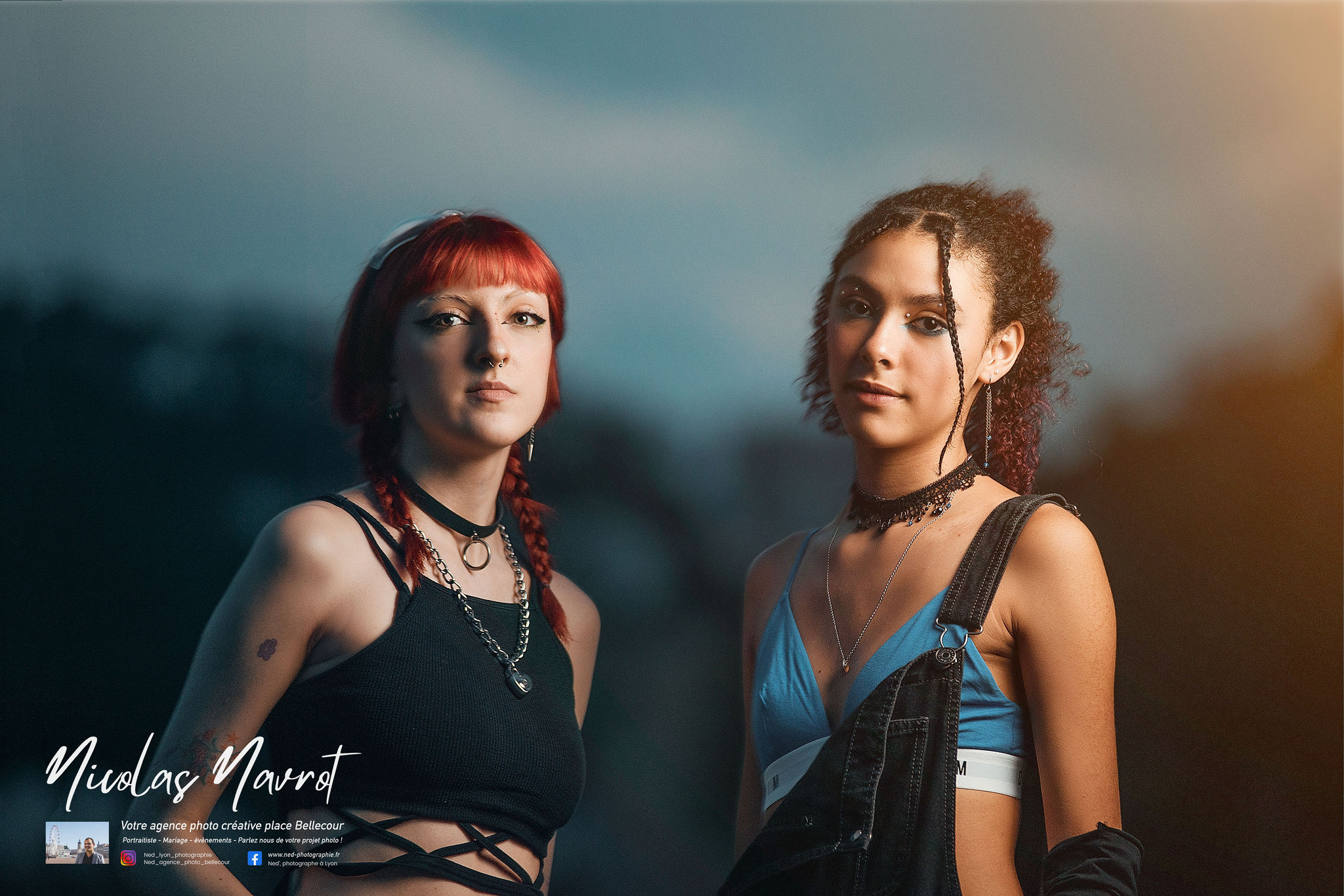 Deux jeunes femmes face à l'appareil photo en studio, l'une aux cheveux rouges vêtue de noir, l'autre aux cheveux bouclés en top bleu, fond dégradé bleu et beige
