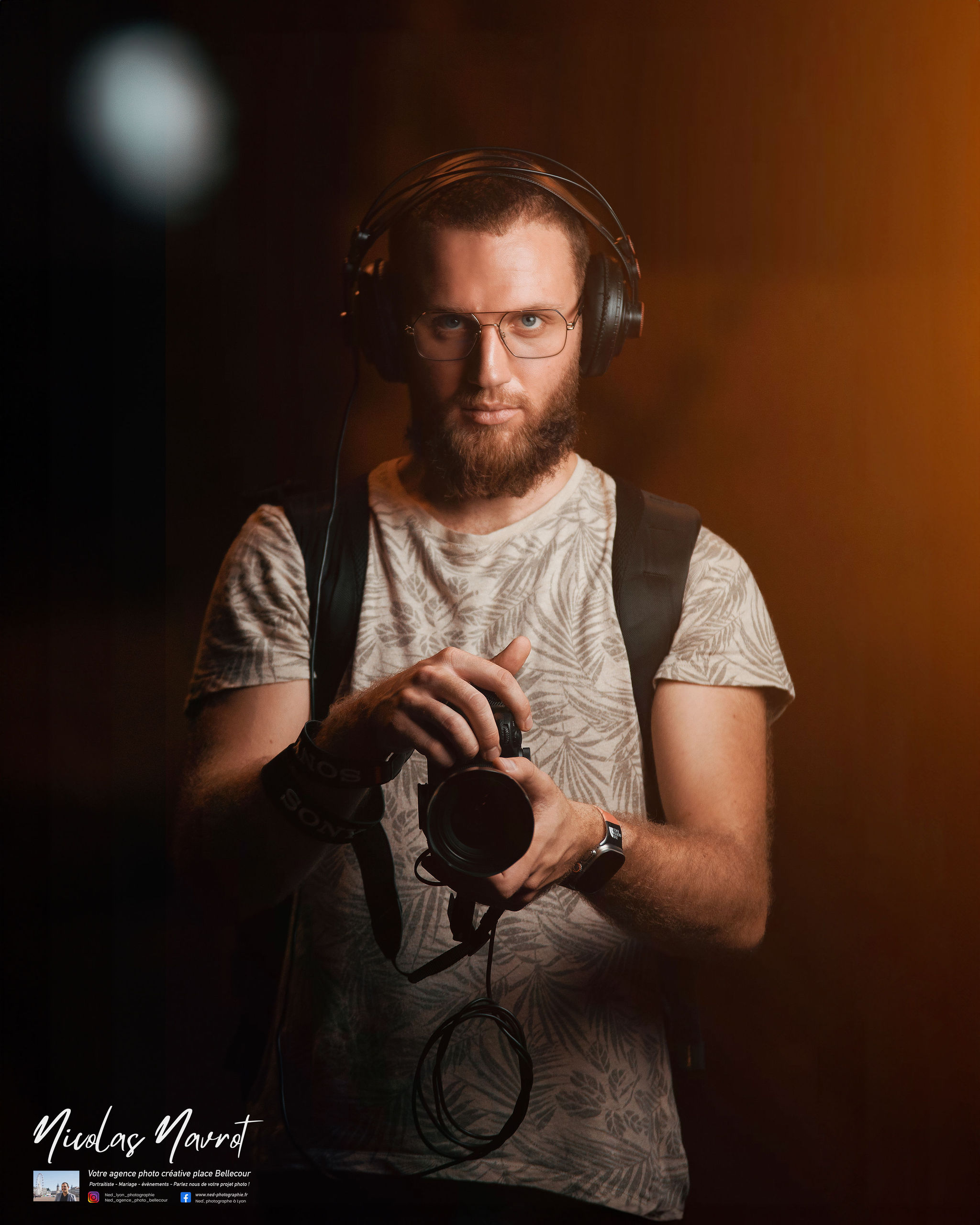 Homme barbu avec lunettes tient un appareil photo reflex, casque audio sur la tete, fond marron studio