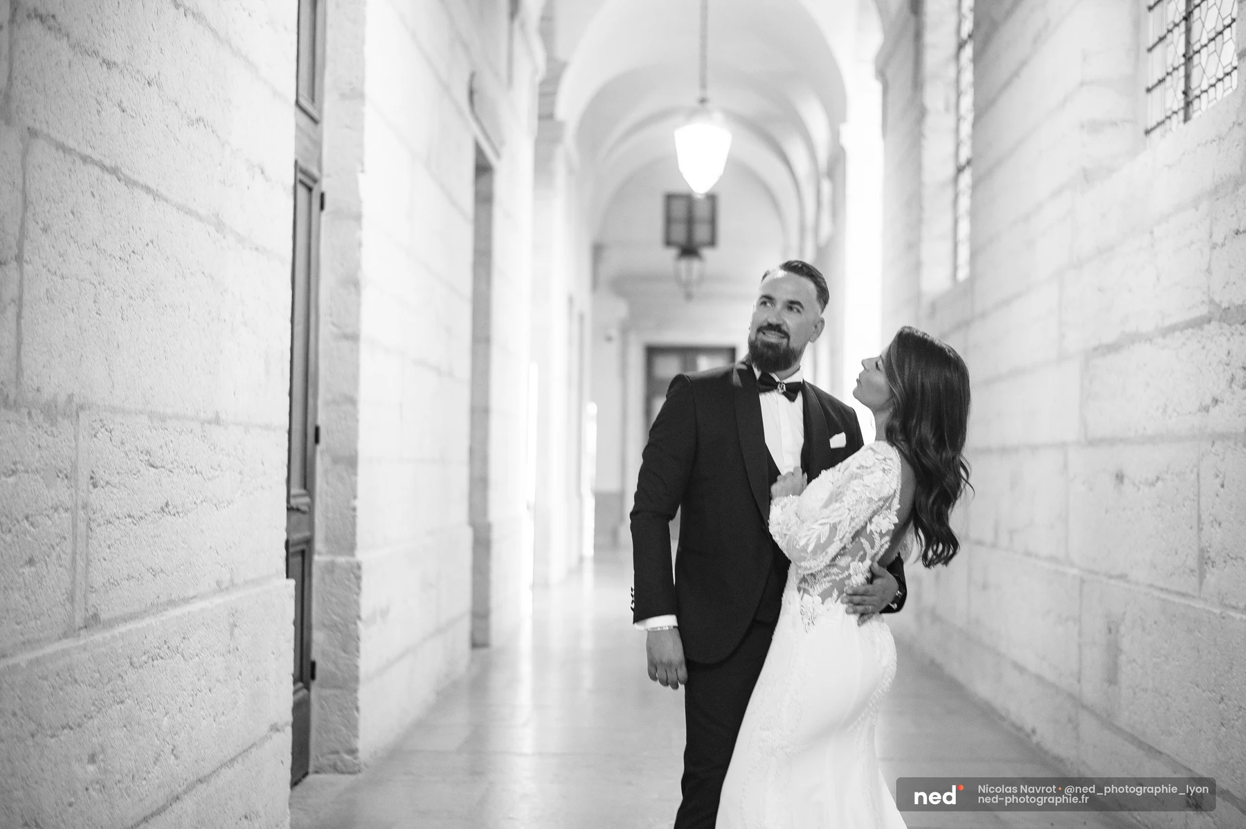 Photo noir et blanc de mariés enlacés dans un couloir voûté en pierre, séance photo couple à Pl. de l'Hôpital