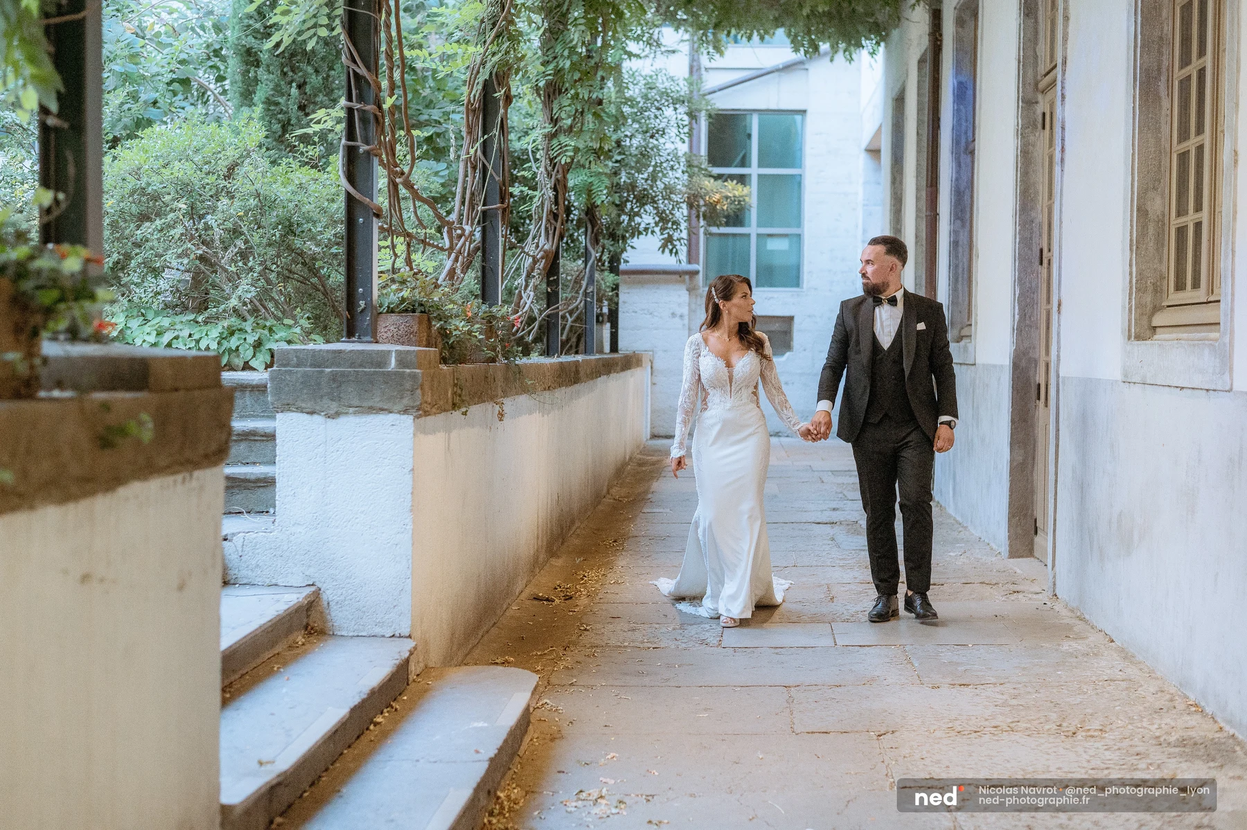 Mariés main dans la main dans un passage verdoyant aux dalles anciennes, séance photo couple à Pl. de l'Hôpital