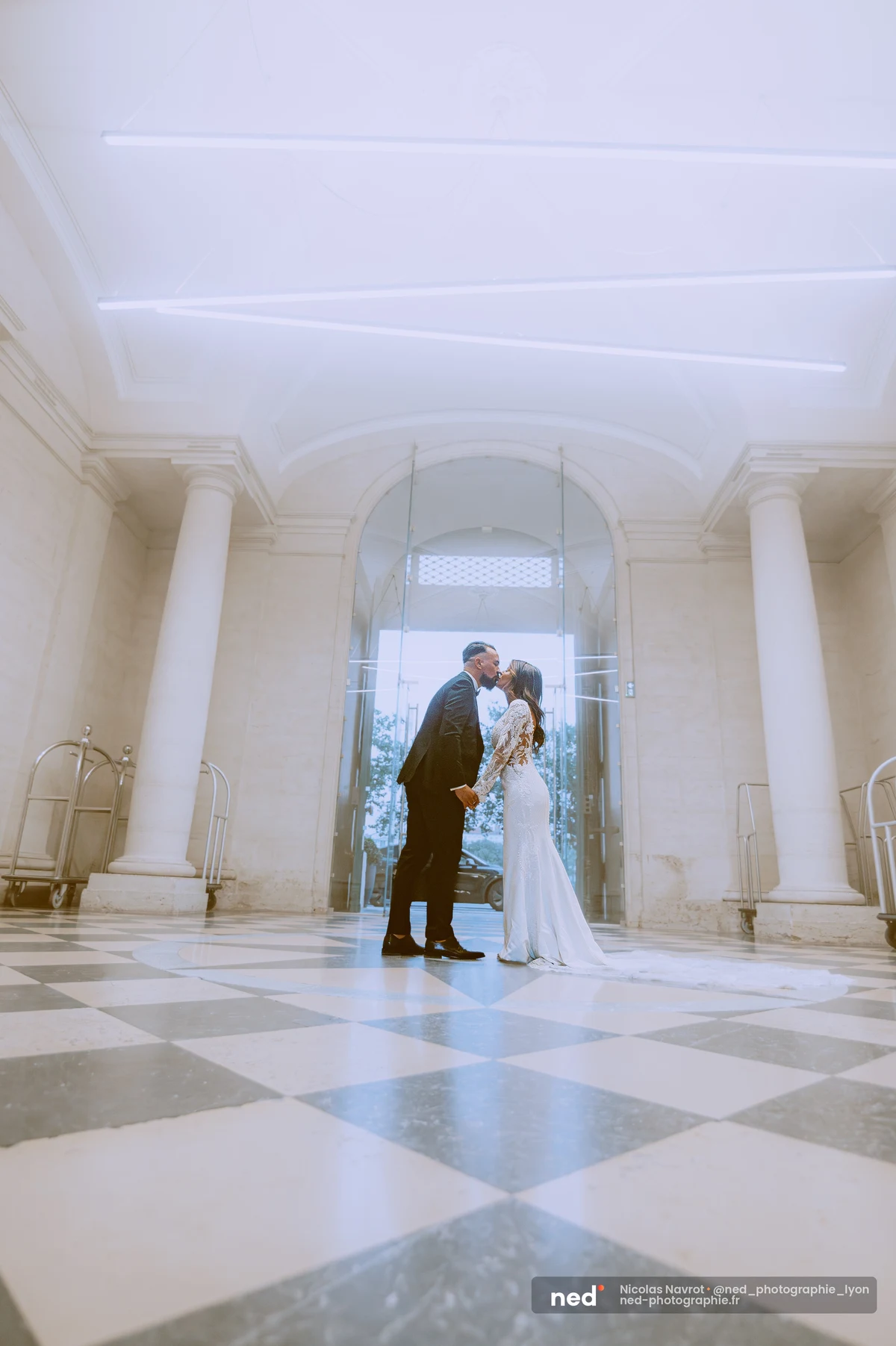 Mariés s'embrassant dans hall d'hôtel carrelage damier vu en contre-plongée, séance photo couple à Pl. de l'Hôpital