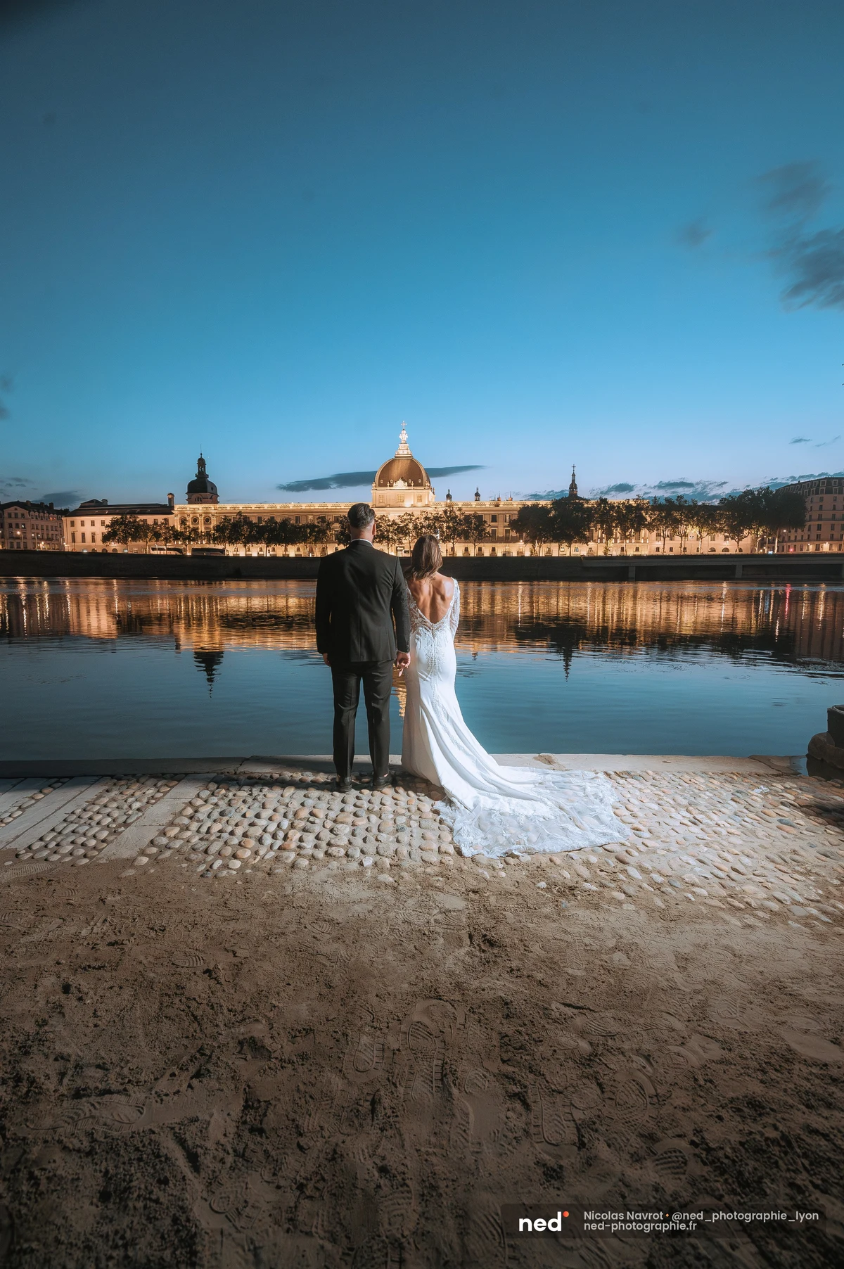 Mariés de dos face au Rhône et à la coupole illuminée de Lyon la nuit, séance photo couple à Pl. de l'Hôpital