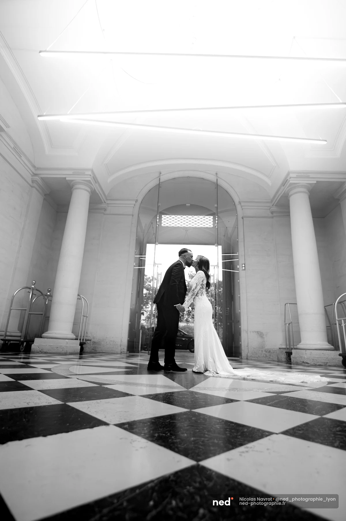 Mariés s'embrassant dans un vestibule à colonnes et sol damier, noir et blanc, séance photo couple à Pl. de l'Hôpital