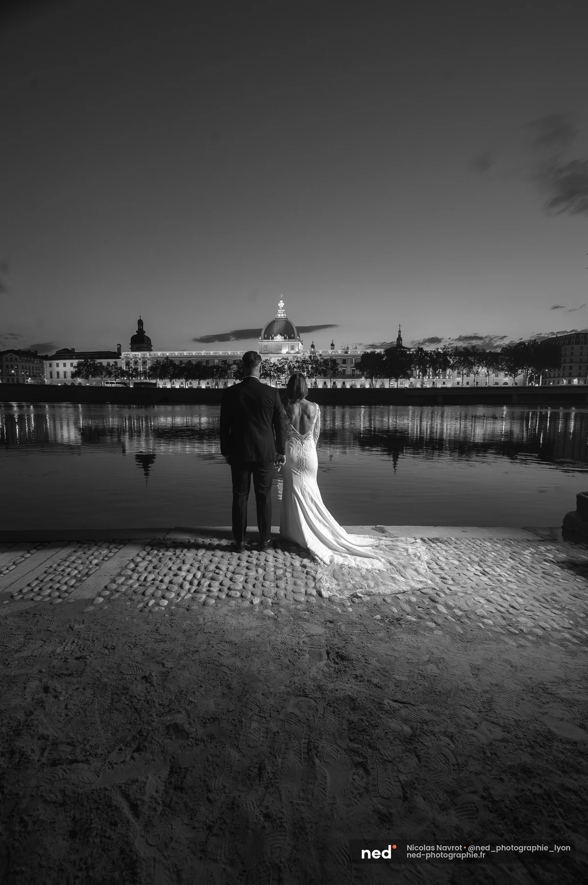 Mariés de dos face au Rhône et à Lyon la nuit, photo noir et blanc, séance photo couple à Pl. de l'Hôpital