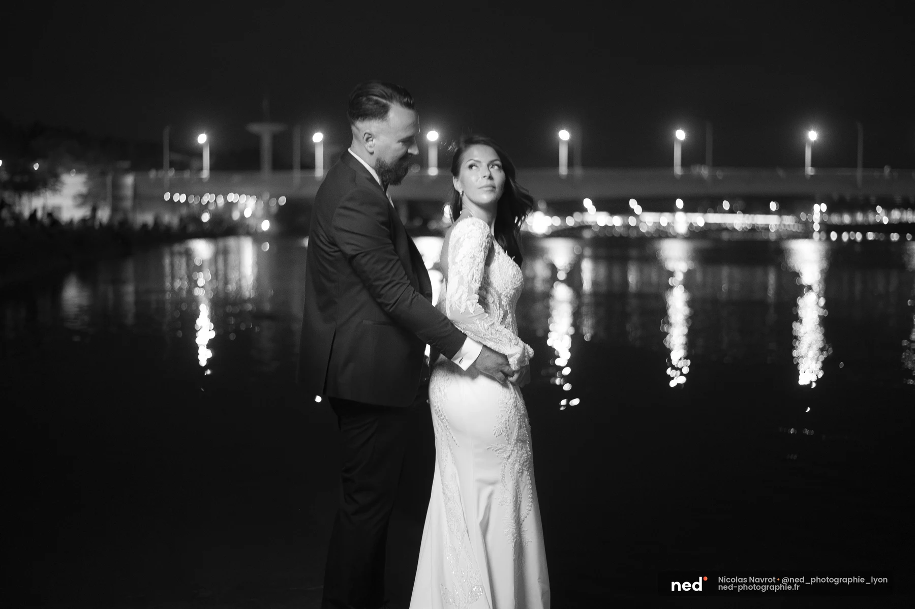 Portrait noir et blanc de mariés au bord de l'eau la nuit, pont illuminé, séance photo couple à Pl. de l'Hôpital