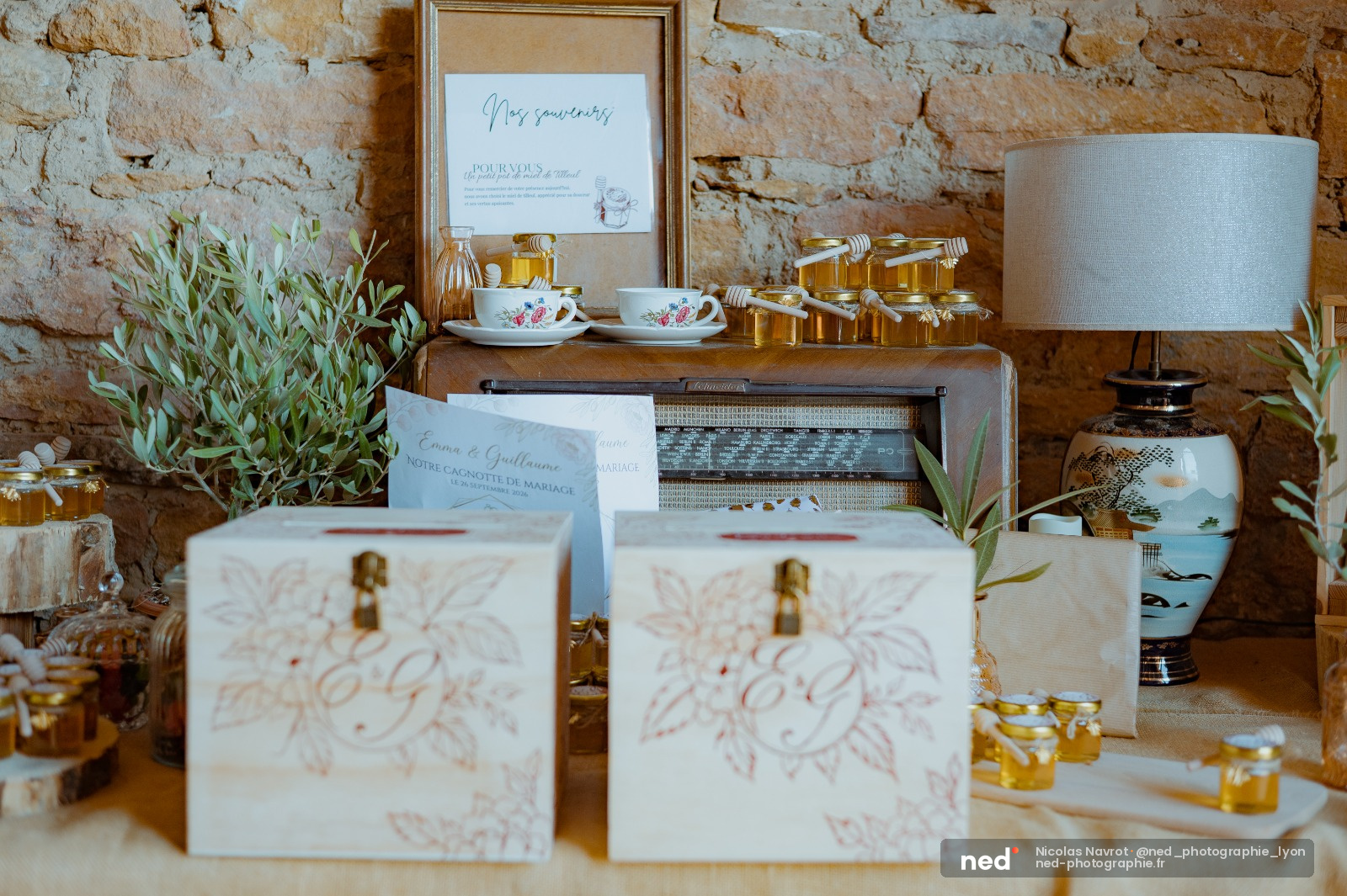 Boites cadeaux blanches avec ruban dore alignees sur une table en pierre, entourees de pots de miel, tasses fleuries et cadre personalise
