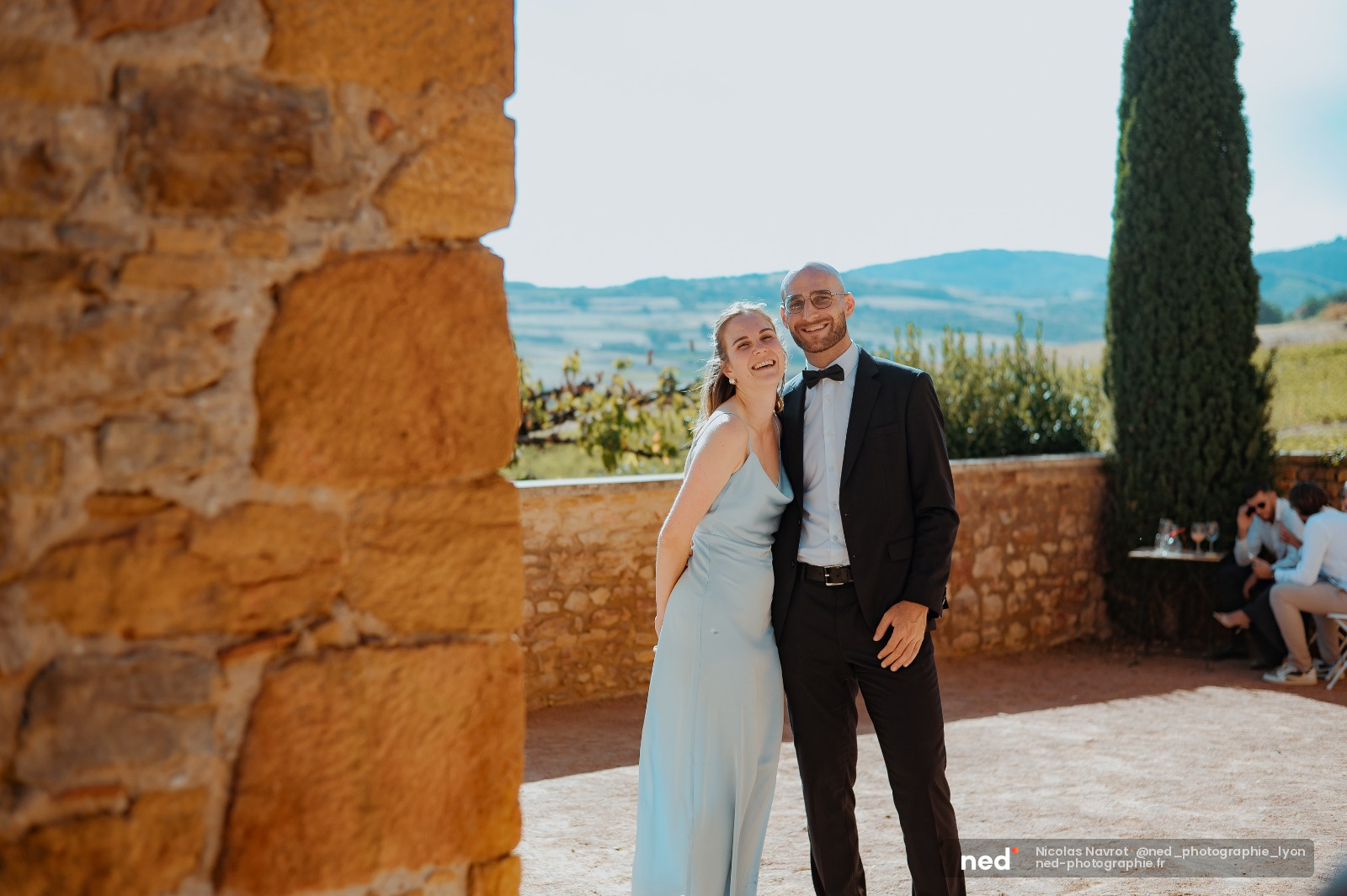 Mariés souriants devant murs en pierre ocre, cyprès et vallée toscane en arrière-plan
