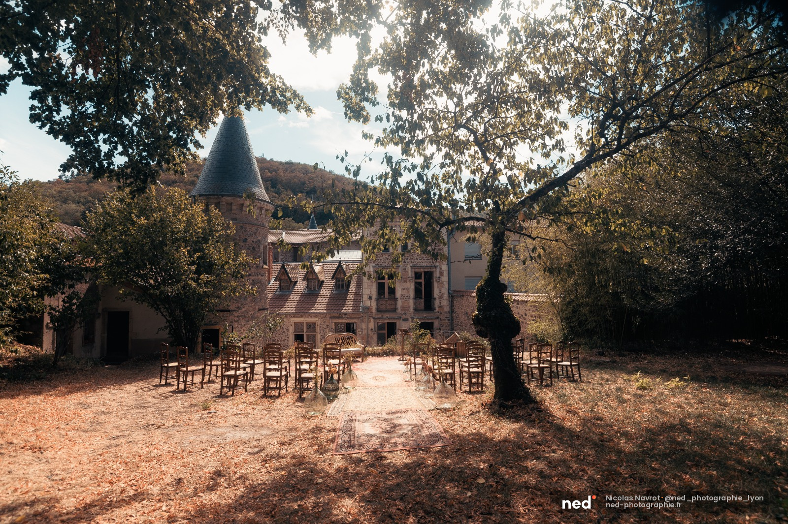 Cour intérieure d'un château en pierre avec chaises disposées pour la cérémonie, feuillage d'automne et tour conique au fond