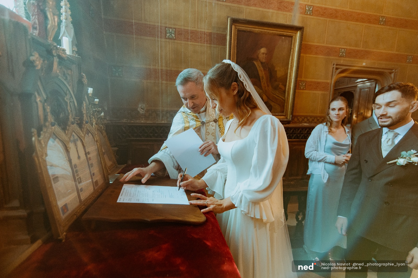 Mariée en robe blanche et voile signe le registre à l'église, le prêtre à ses côtés, famille présente en arrière-plan