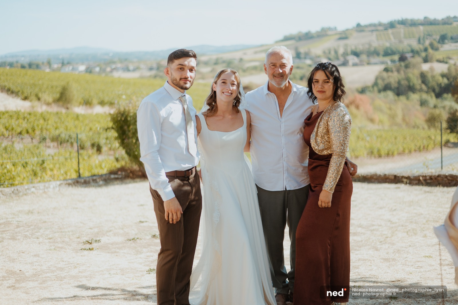 Mariée en robe blanche avec trois membres de sa famille souriants dans les vignes, lumière naturelle de jour
