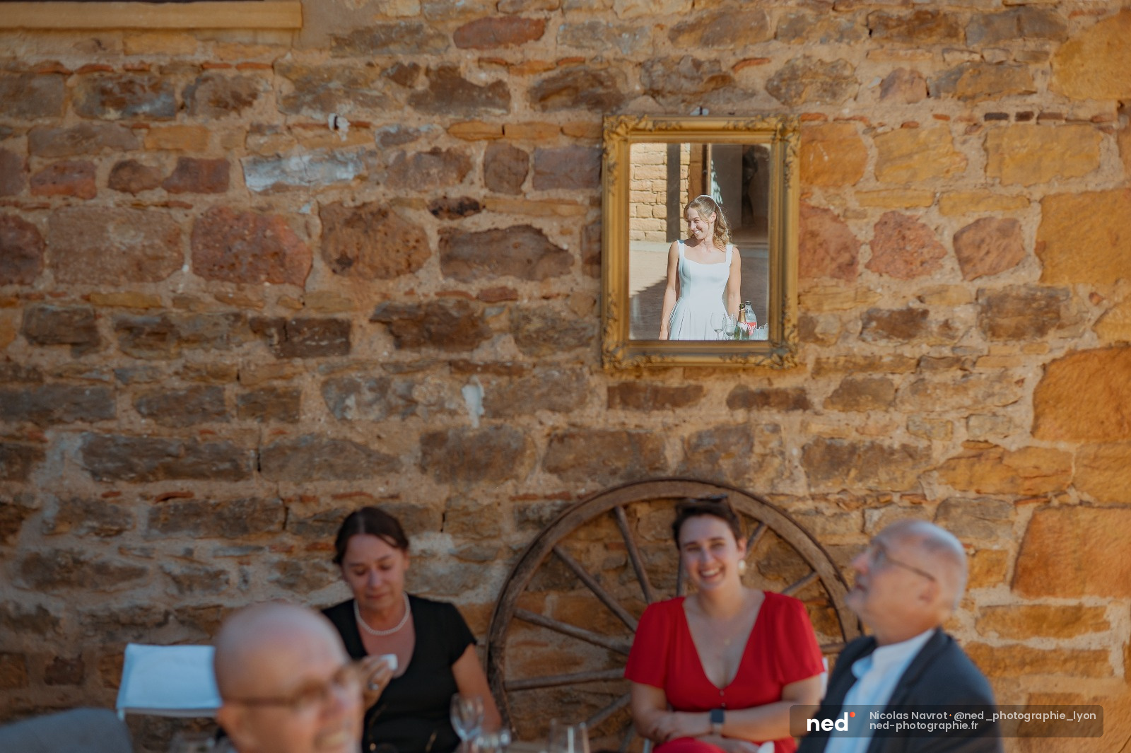 Mariée en robe blanche posant devant une fenêtre, son portrait encadré d'or accrochée au mur en pierre d'une salle de réception