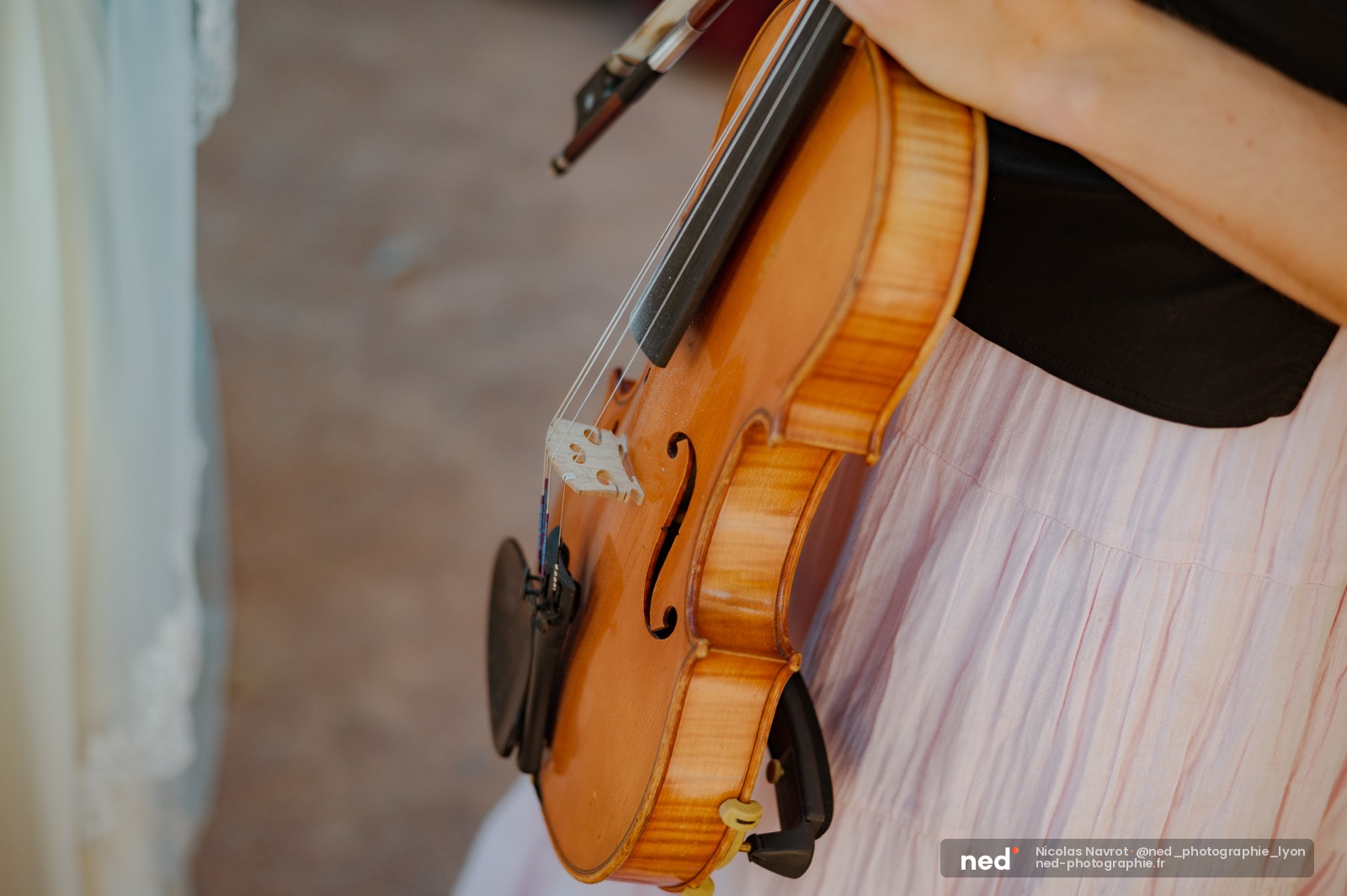 Mariée en robe rose pâle tenant un violon en bois clair, détail du corps de l'instrument avec archet
