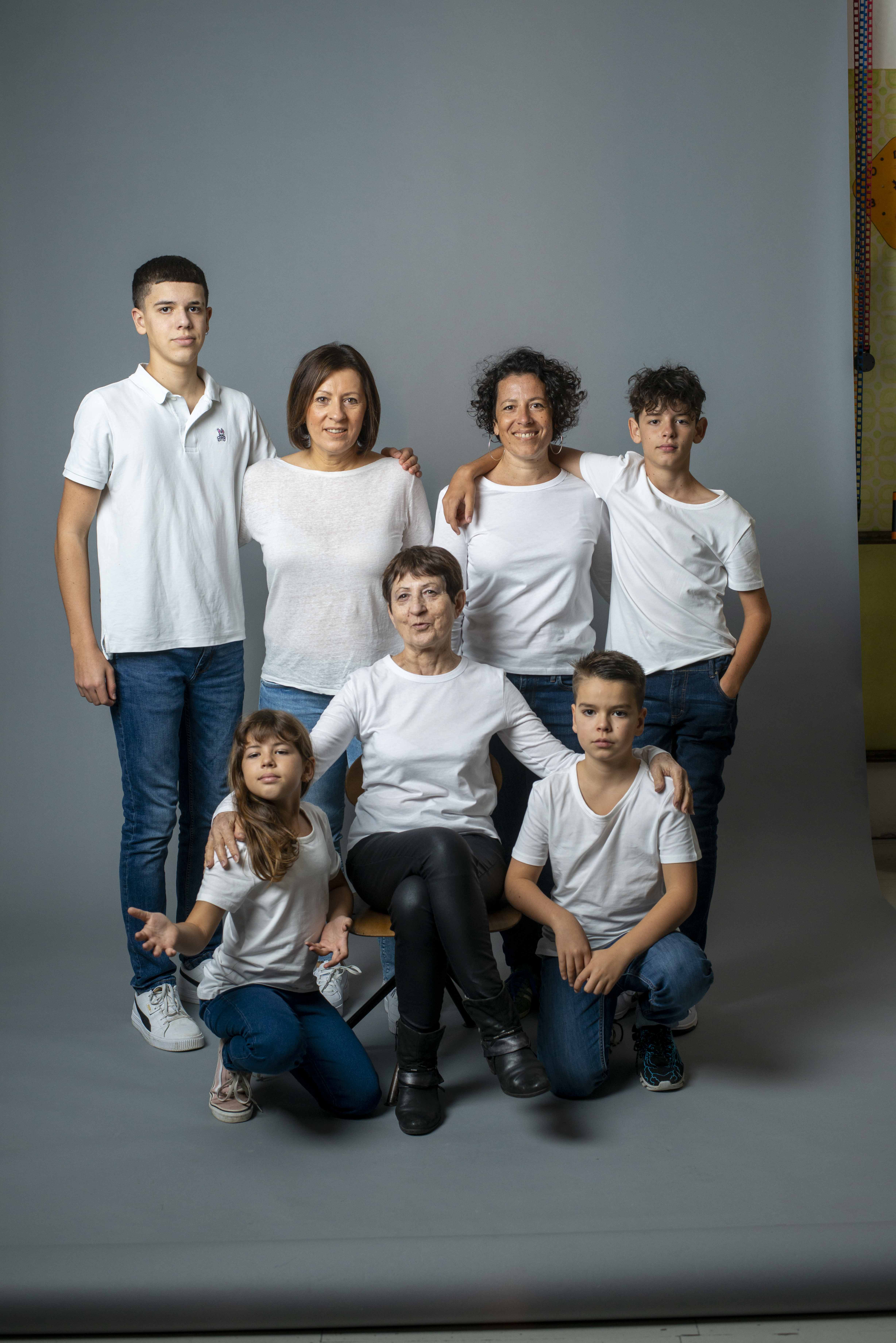 Famille de sept personnes posant ensemble en tenues blanches et bleues devant un mur gris, trois générations réunies